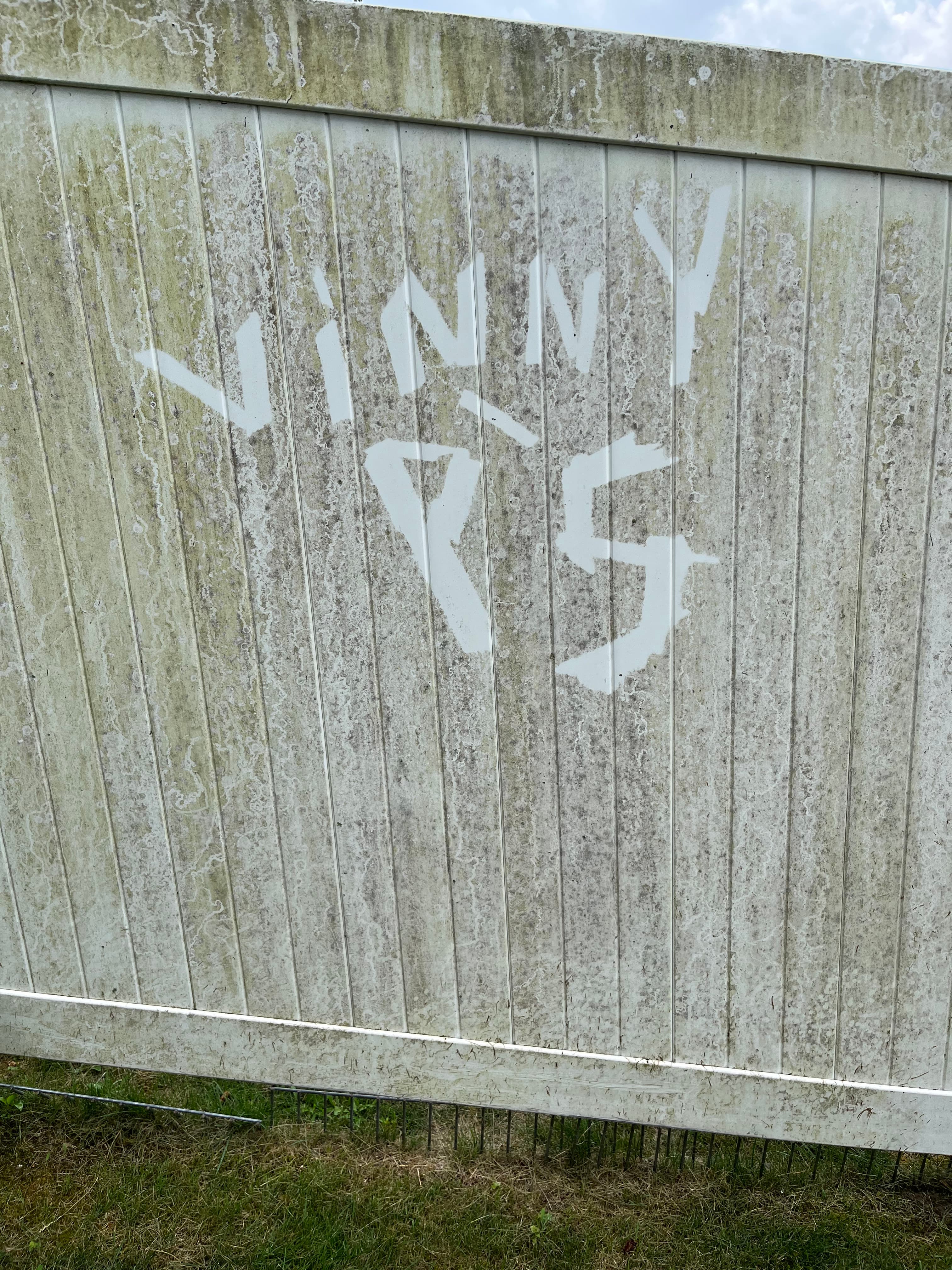'Vinny P's' pressure-washed into a dirty fence — a before-and-after captured in a single frame